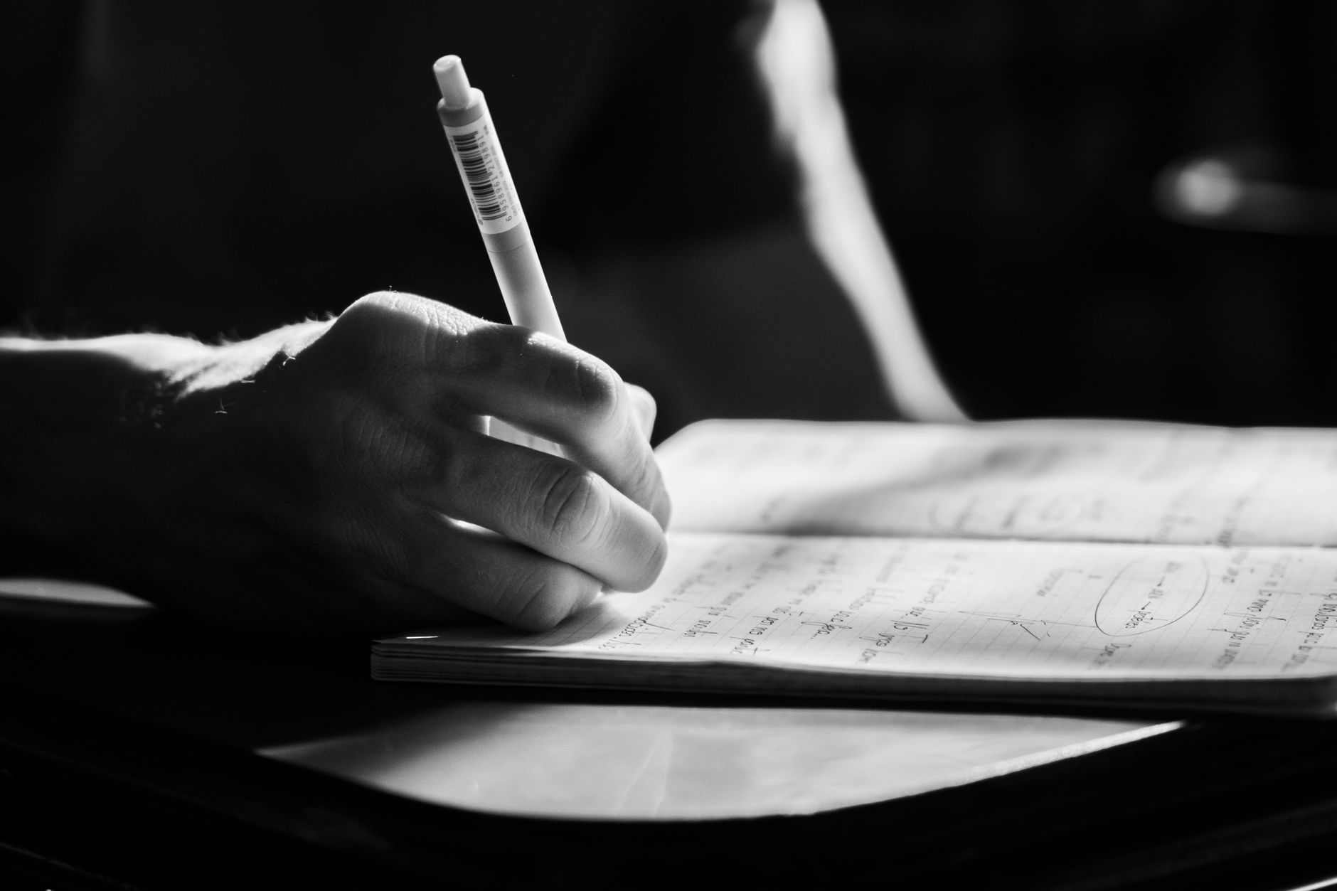 black and white close up of hand writing in notebook